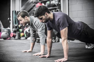 Two mid adult men doing high planks in gym.