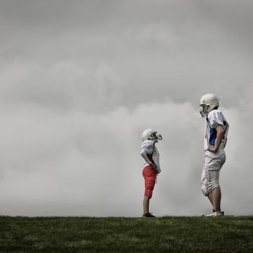 two people facing each other, one very tall football player, and one much shorter person looking up, hands on hips 