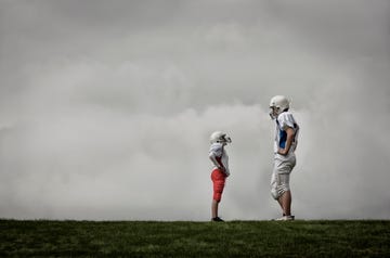 two people facing each other, one very tall football player, and one much shorter person looking up, hands on hips 