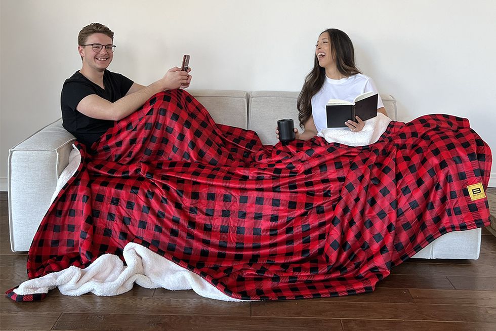 two people sharing big blnket cos giant red and black sherpa blanket on a couch