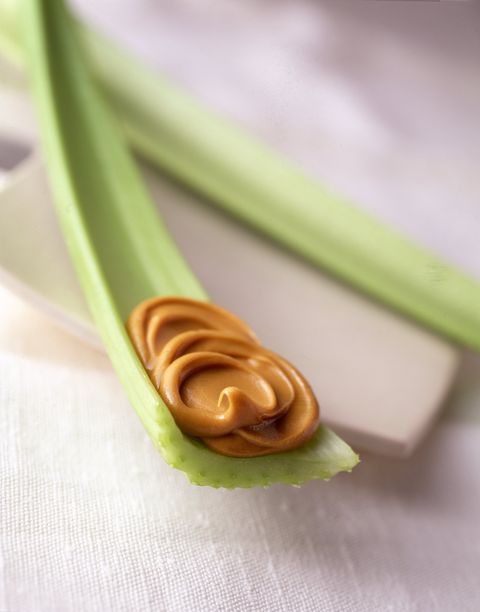 Two pieces of celery with a dollop of peanut butter on the end against a white background