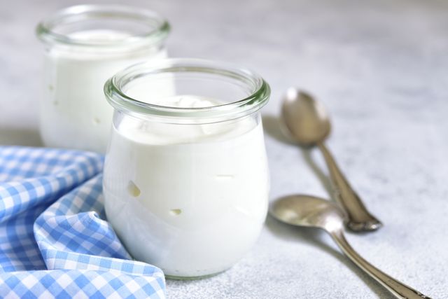 two portions of fresh natural  homemade organic yogurt in a glass jar on a light slate background