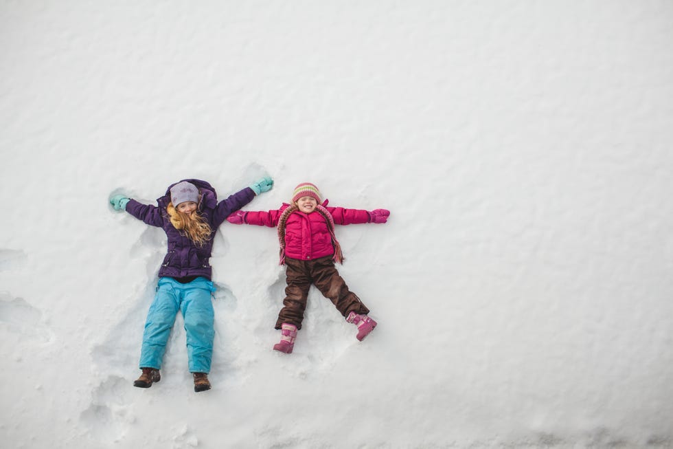 two sisters playing, making snow angels in snow