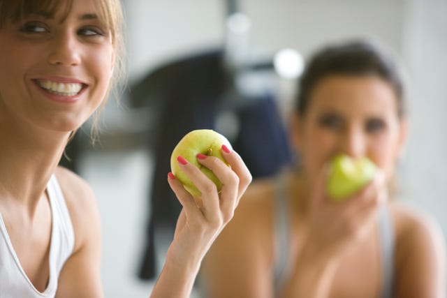 two smiling women eating apples defocused