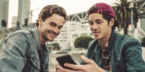 Two smiling young men sharing cell phone outdoors