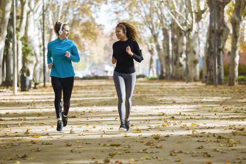 Two smiling young women running in park listening to music
