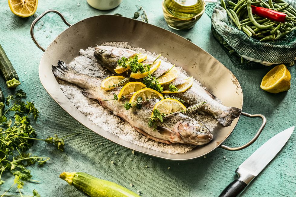 Two trout stuffed with herbs and lemon slices in fish pan