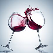 Two wine glasses in toasting gesture with big splashing. Alcohol concept. Two glasses of wine on the gray background