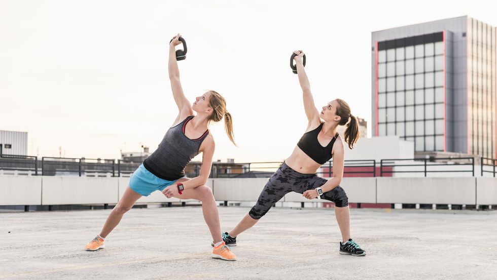 Two women exercising with kettlebells on parking level in the city