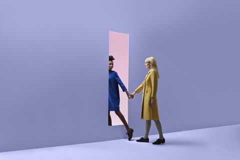 two women holding hands, walking threw rectangular opening in coloured wall