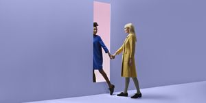 two women holding hands, walking threw rectangular opening in coloured wall