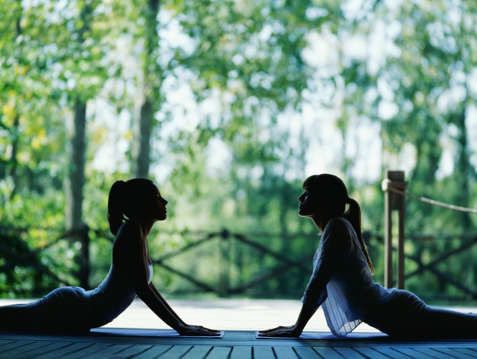 two women performing yoga on terrace, side view