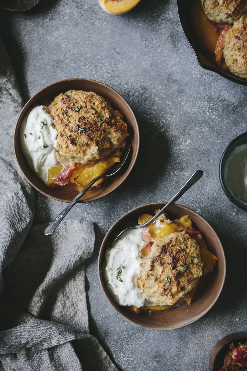 Two wood bowls filled with peach cobbler and honey swirled ricotta and thyme are photographed from the top view.