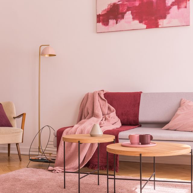 two wooden coffee tables next to modern grey sofa with pillows and blankets in lovely pastel pink living room interior