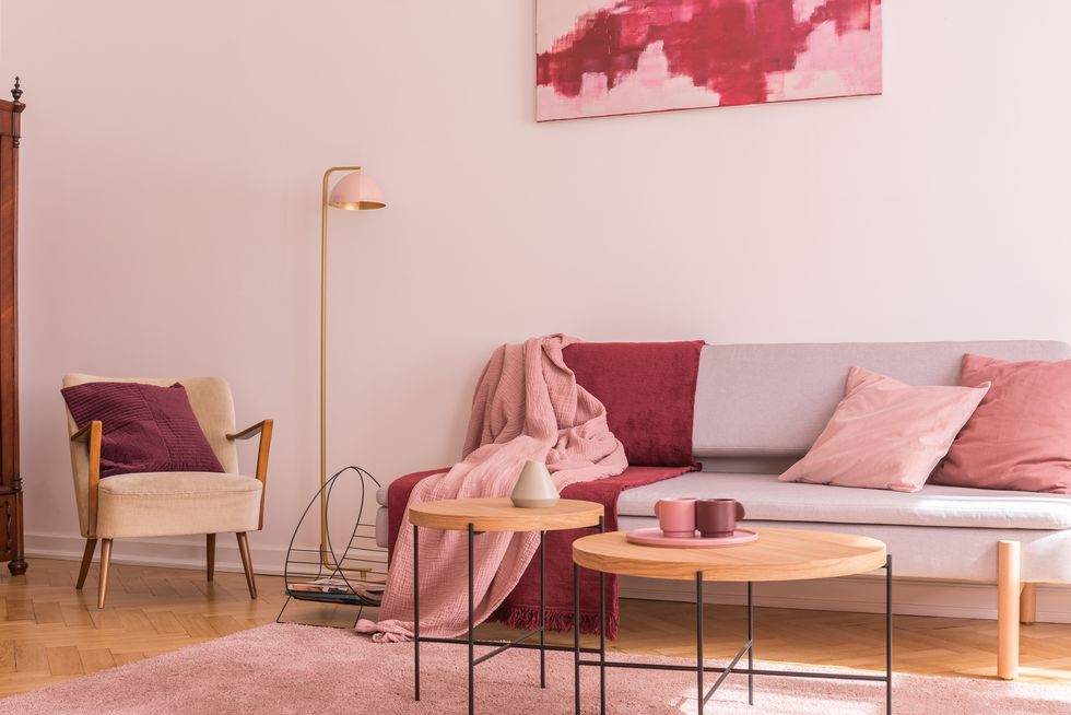 two wooden coffee tables next to modern grey sofa with pillows and blankets in lovely pastel pink living room interior