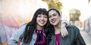 Two Young Latina Women Leaning Together, Smiling and Happy