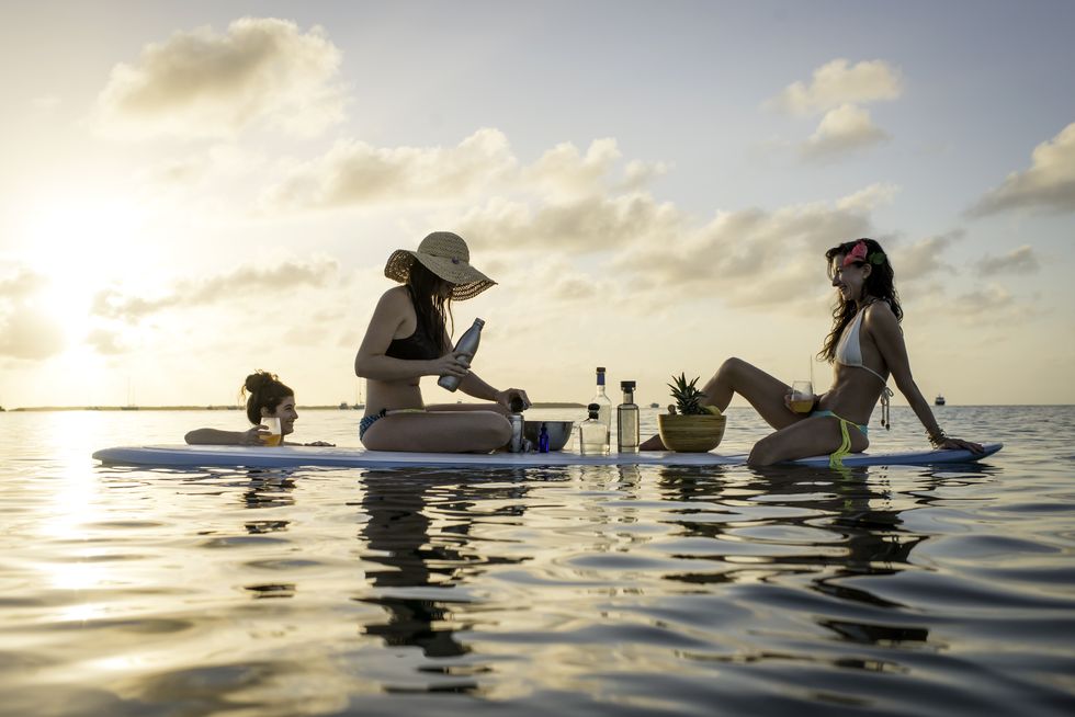 two young women preparing cocktails on paddleboard at sunset