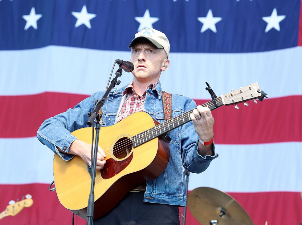 tyler childers playing a guitar while performing at a concert in front of a giant american flag