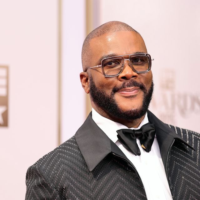 man in a tuxedo and bowtie with chunky frame glasses smiles as he looks left