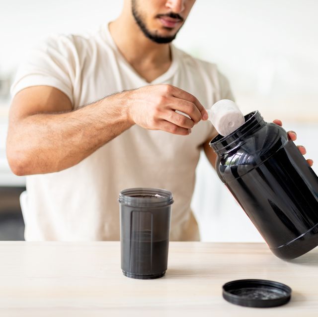 unrecognizable young sporty guy making protein shake at table in kitchen, closeup cropped view of millennial bodybuilder using sports nutrition supplement, preparing cocktail indoors