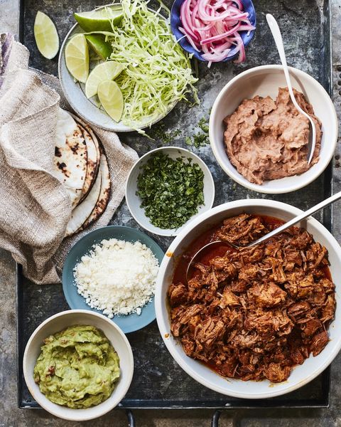 cochinita pibil in bowl with small bowls of toppings and tortillas on side