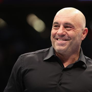 joe rogan smiles and looks to the left, he wears a black collared shirt