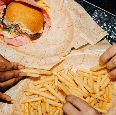 two hands reaching for a shared plate of fries with a burger also in shot
