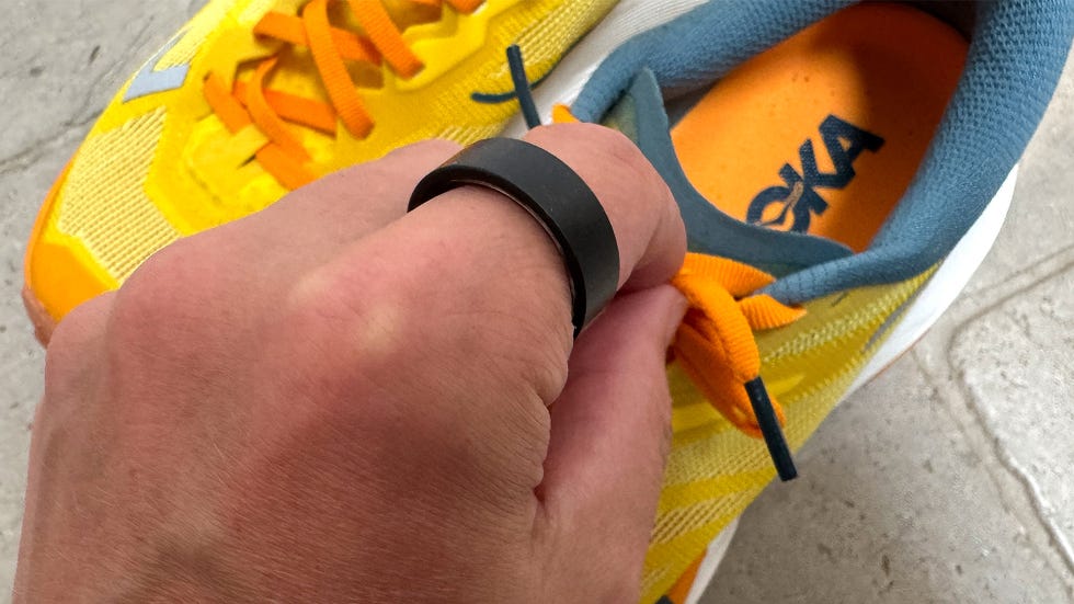 a hand wearing a black smart ring as they tie a pair of yellow trainers