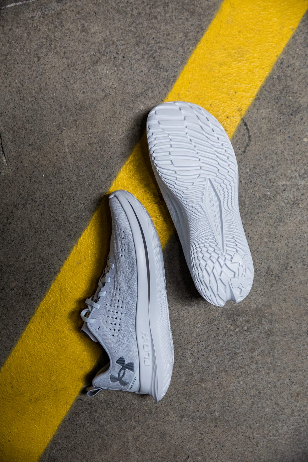 under arour velociti 4 running shoes positioned on a concrete surface with a yellow line