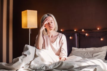 unhappy sad middle aged woman sitting on bed at home