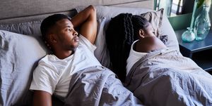 unhappy young man lying in bed next to his sleeping wife