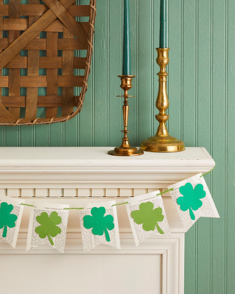 a banner made from book pages cut into the shape of flags with green paper four leaf clovers attached to the front hung on a mantel