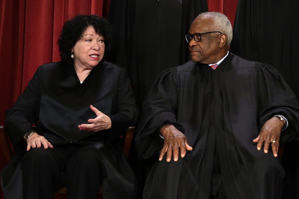sonia sotomayor speaks to clarence thomas, both of whom are seated and wearing black judge robes