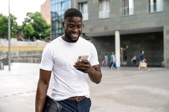 man in a white tshirt walking while looking at his phone