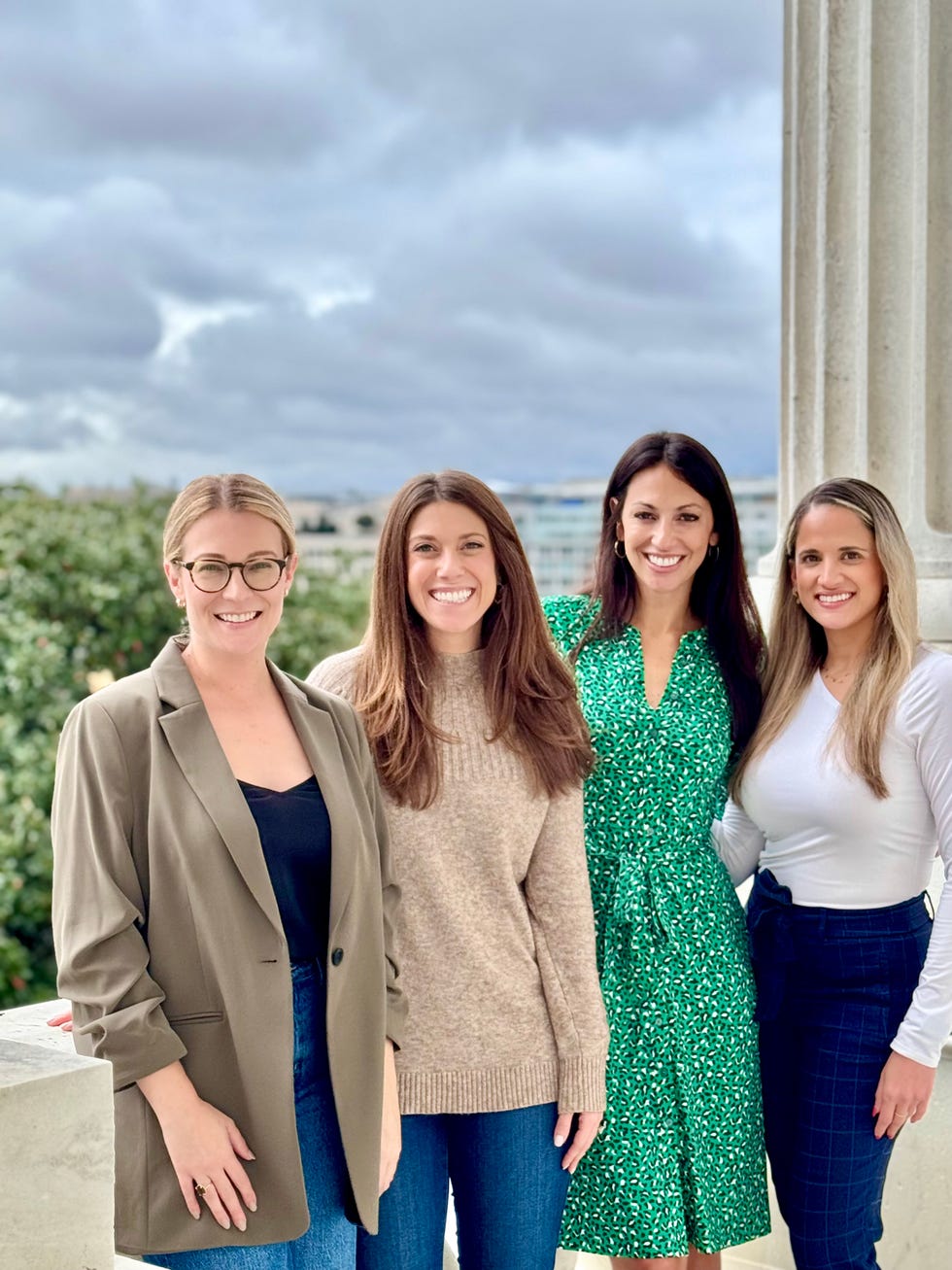 four women standing together outdoors with a cloudy sky in the background