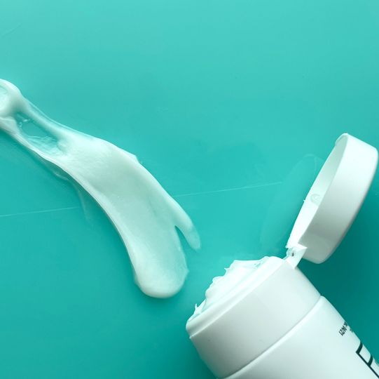 a squeeze of white diaper rash cream, shown along with its bottle on a teal background, part of a good housekeeping test of the best diaper rash creams
