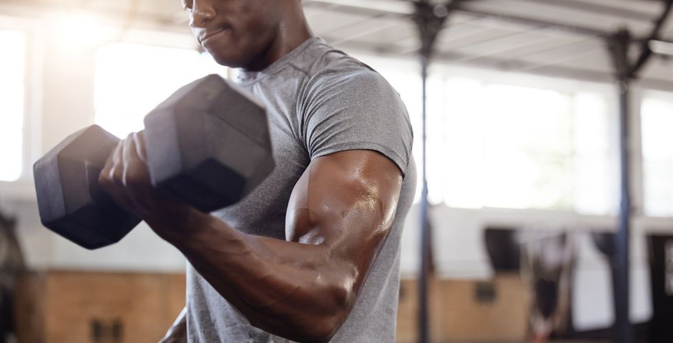 unknown african american athlete lifting dumbbell during bicep curl arm workout in gym. strong, fit, active black man training with weight in health and sports club. weightlifting exercise routine