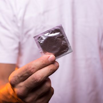 unknown man in white shirt holding condom in hand