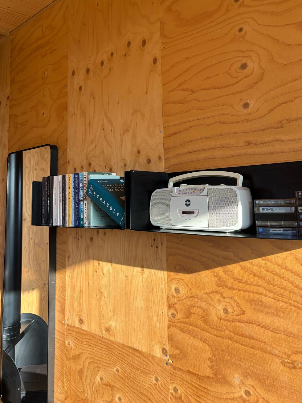 a wooden wall with a black shelving unit displaying a white radio, tapes and several books