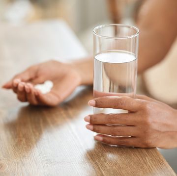 unrecognizable black woman takes medicines with glass of water at home