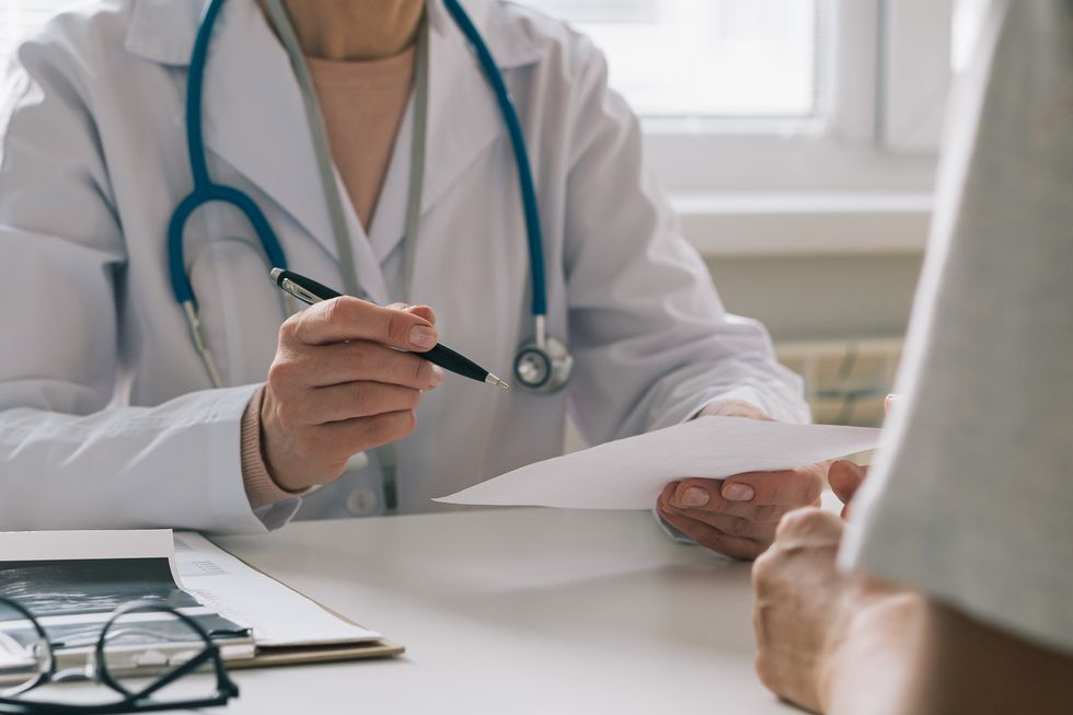 unrecognizable doctor consulting patient giving piece of paper with instructions and recommendations