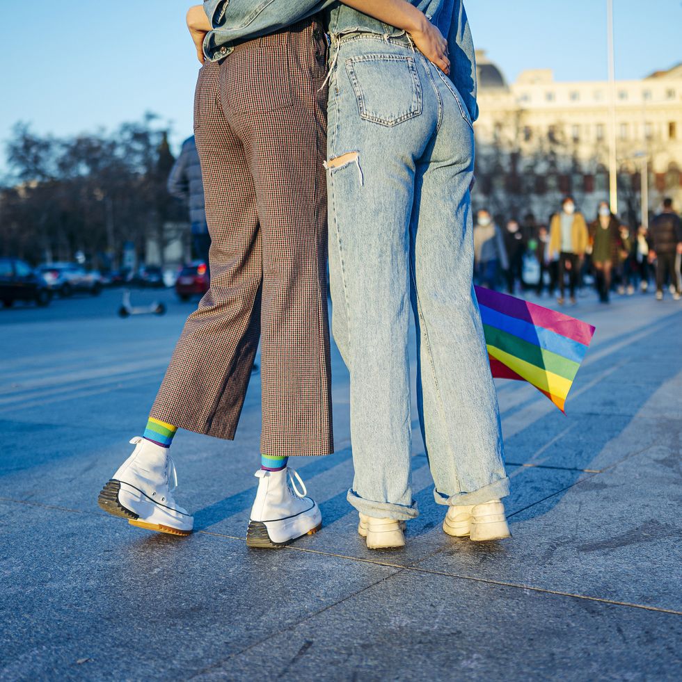 unrecognizable lesbian female couple with gay pride flag in madrid city street