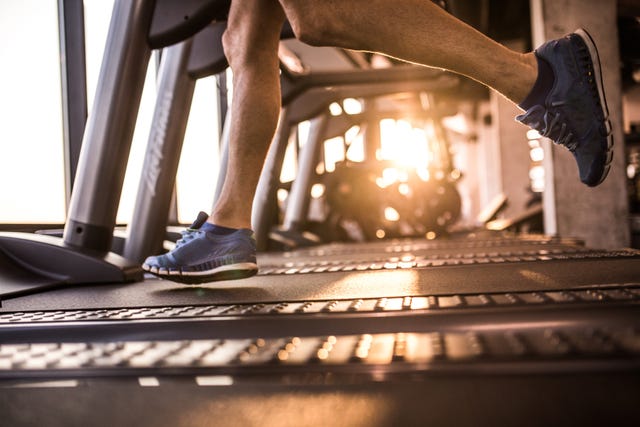 unrecognizable male athlete running on treadmill in health club