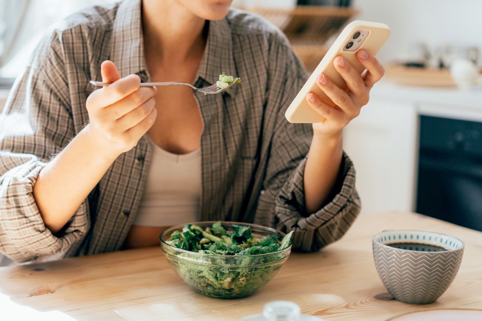 unrecognizable modern woman having breakfast with salad and scrolling the news feed in her phone