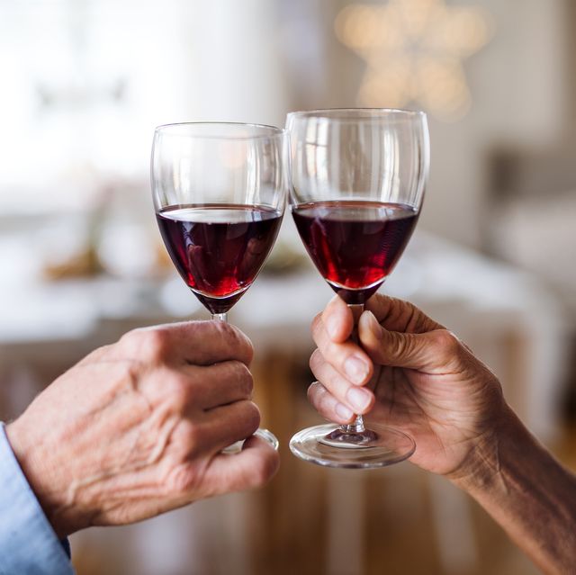unrecognizable senior couple holding wine indoors at christmas time, clinking glasses