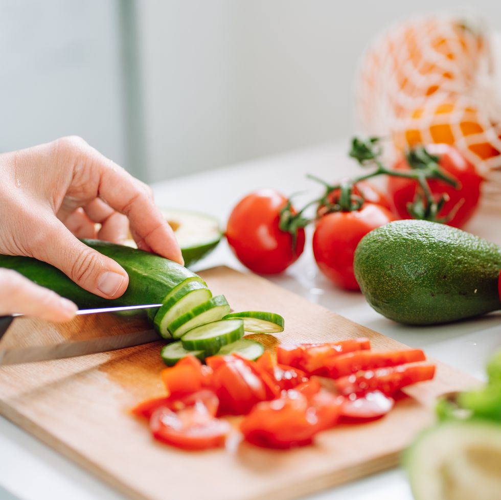 unrecognizable woman hands cutting zucchini on wooden chopping board on the table