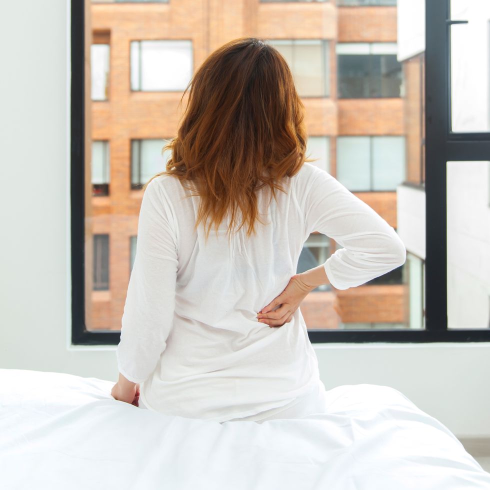 unrecognizable woman sitting on bed with a back pain