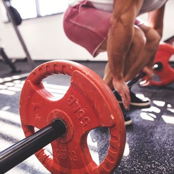 Unrecognizable young fit man in gym working out with heavy barbell, doing dead lift