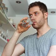 unshaven man drinks water from a glass in the kitchen