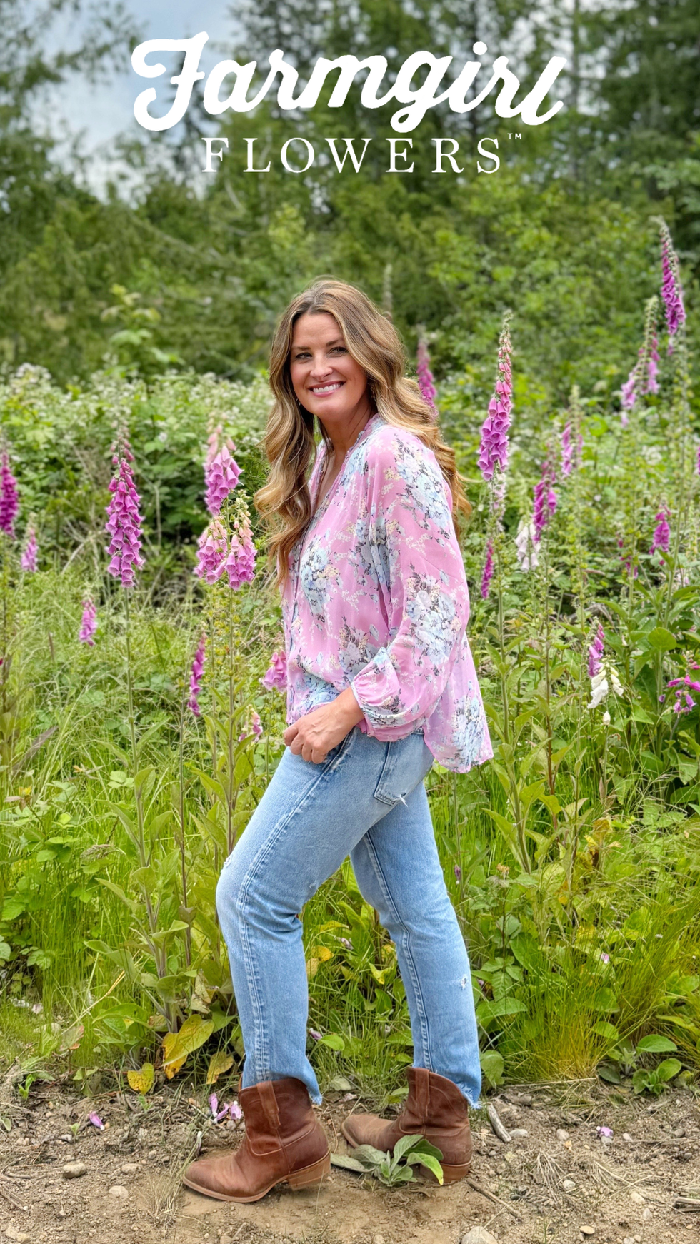 woman standing among flowers wearing a floral blouse and jeans